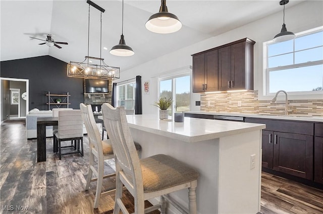 kitchen with dark brown cabinetry, a kitchen island, open floor plan, decorative light fixtures, and a sink