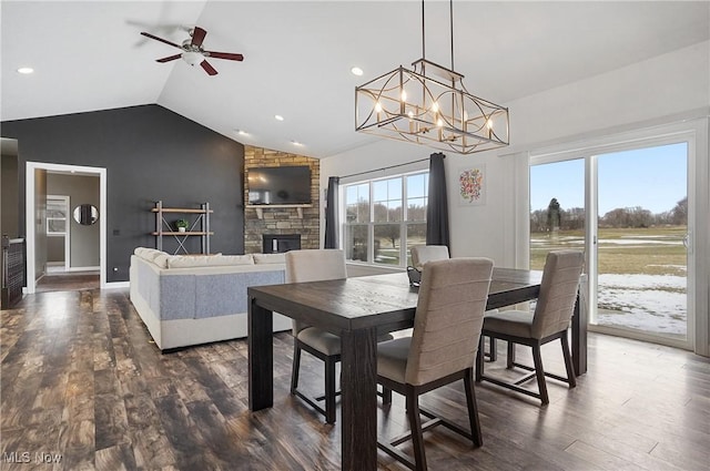 dining room with baseboards, lofted ceiling, dark wood-type flooring, a stone fireplace, and recessed lighting