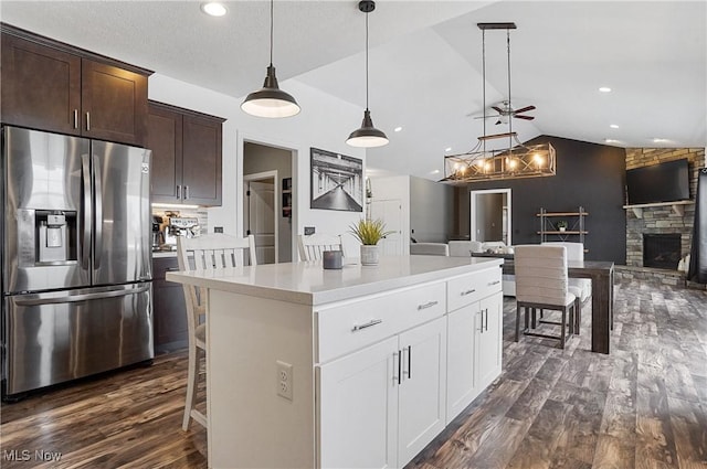 kitchen with decorative light fixtures, stainless steel refrigerator with ice dispenser, open floor plan, white cabinets, and a kitchen island