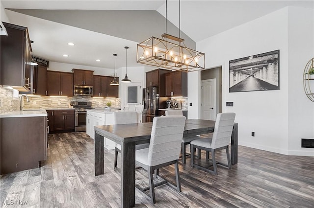 dining room with baseboards, wood finished floors, an inviting chandelier, high vaulted ceiling, and recessed lighting