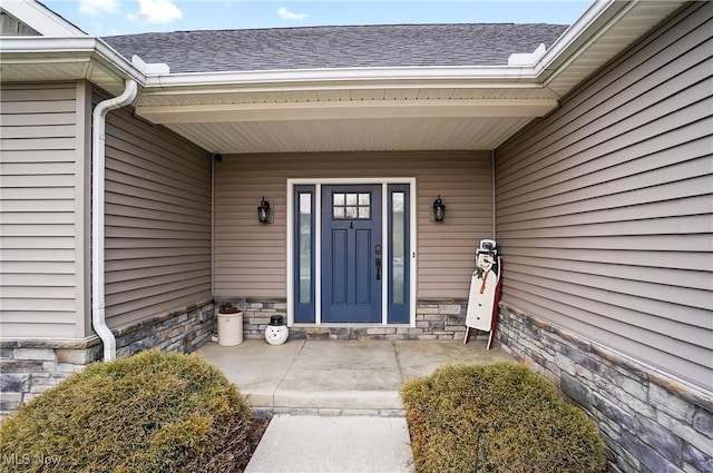 view of exterior entry featuring stone siding and roof with shingles