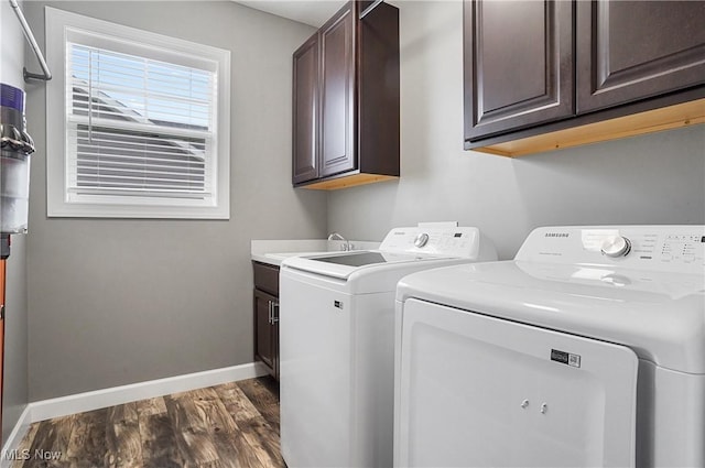 clothes washing area with dark wood finished floors, washer and clothes dryer, cabinet space, a sink, and baseboards