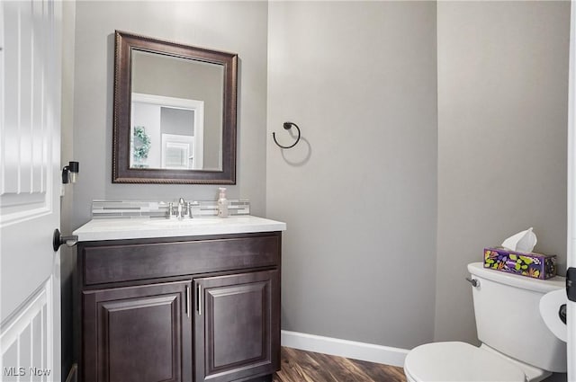 half bathroom with toilet, wood finished floors, vanity, and baseboards