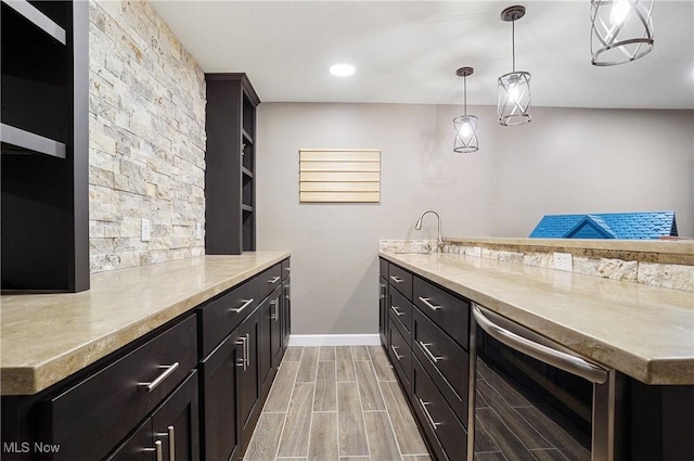 kitchen featuring wine cooler, pendant lighting, wood finish floors, light countertops, and a sink