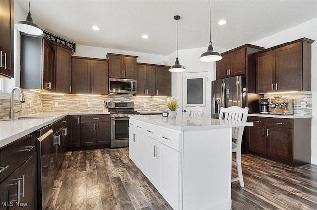 kitchen with stainless steel appliances, a sink, hanging light fixtures, light countertops, and a center island