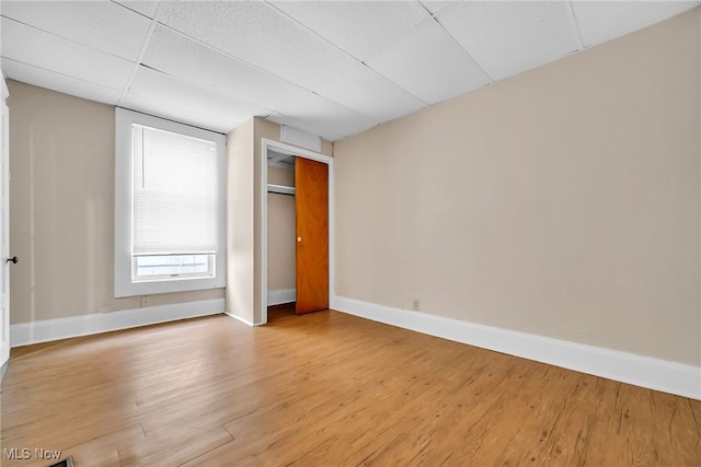 spare room featuring light wood-style floors, a drop ceiling, and baseboards