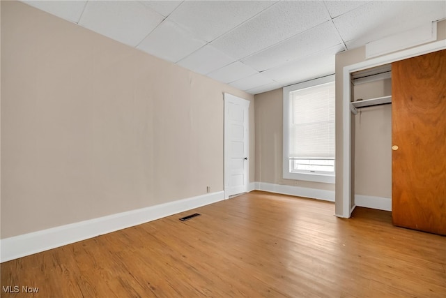 unfurnished bedroom with a closet, visible vents, light wood-style flooring, a drop ceiling, and baseboards