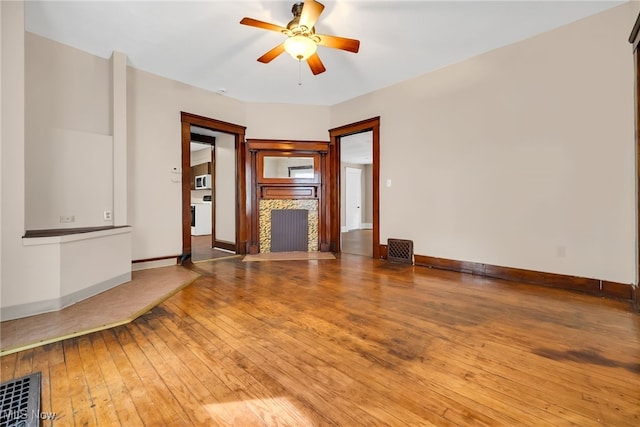 unfurnished living room with a fireplace, a ceiling fan, visible vents, baseboards, and hardwood / wood-style floors