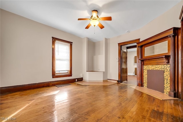 unfurnished living room featuring baseboards, visible vents, hardwood / wood-style flooring, ceiling fan, and a fireplace