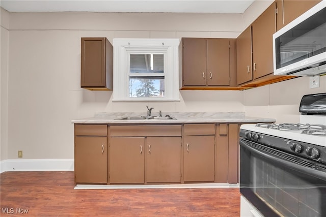 kitchen with gas range, light countertops, a sink, and wood finished floors