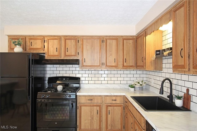 kitchen featuring a sink, black appliances, light countertops, and decorative backsplash