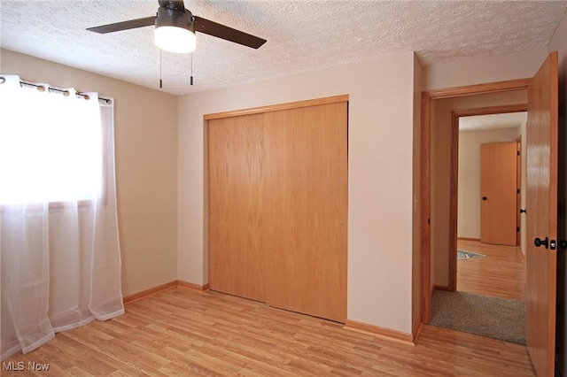 unfurnished bedroom featuring light wood-type flooring, a closet, a textured ceiling, and baseboards