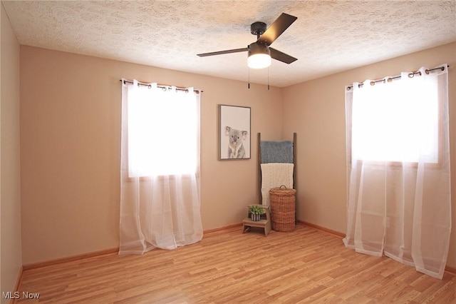 unfurnished room featuring a textured ceiling, ceiling fan, light wood-style flooring, and baseboards