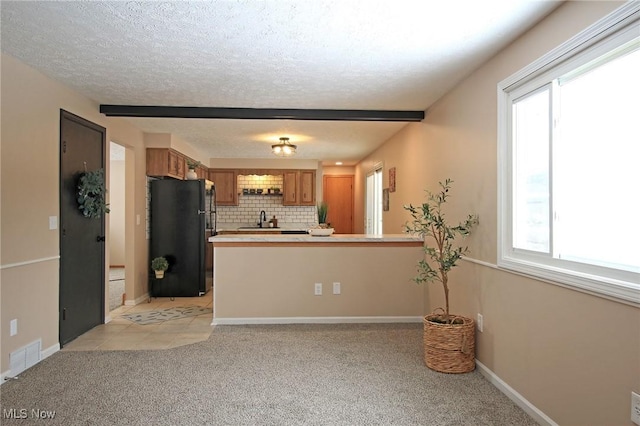 kitchen featuring light colored carpet, a peninsula, light countertops, freestanding refrigerator, and brown cabinets