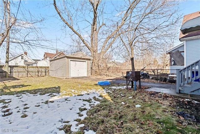 yard layered in snow featuring a garage, an outbuilding, a fenced backyard, and a shed