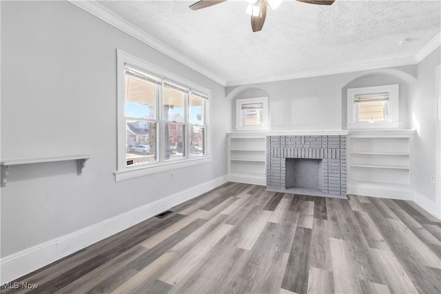 unfurnished living room featuring ornamental molding, a brick fireplace, a textured ceiling, wood finished floors, and baseboards