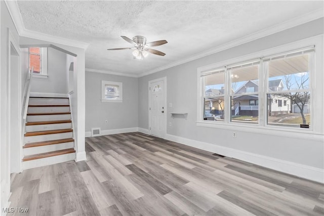 interior space with a textured ceiling, ornamental molding, light wood-type flooring, and stairs