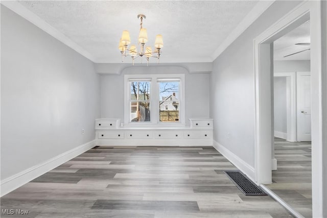 unfurnished dining area featuring baseboards, visible vents, a notable chandelier, and wood finished floors