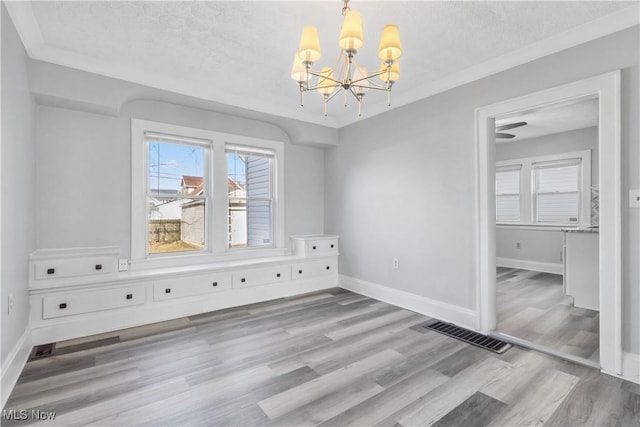 unfurnished dining area featuring baseboards, visible vents, wood finished floors, a textured ceiling, and a chandelier