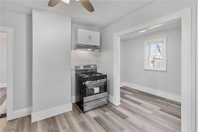 kitchen featuring baseboards, white cabinets, decorative backsplash, under cabinet range hood, and gas stove