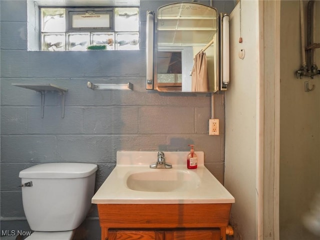 bathroom featuring toilet, concrete block wall, and vanity