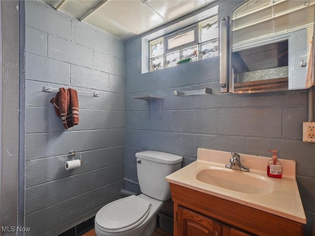 half bath with vanity, toilet, and concrete block wall