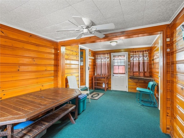 sitting room with carpet floors, wood walls, and a ceiling fan