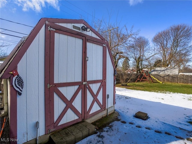 snow covered structure with a playground, fence, an outdoor structure, and a shed