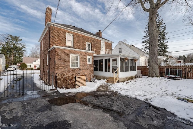 snow covered property featuring a sunroom, a chimney, fence, and brick siding