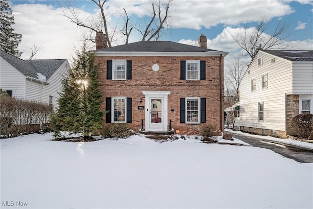 colonial house featuring a chimney and brick siding