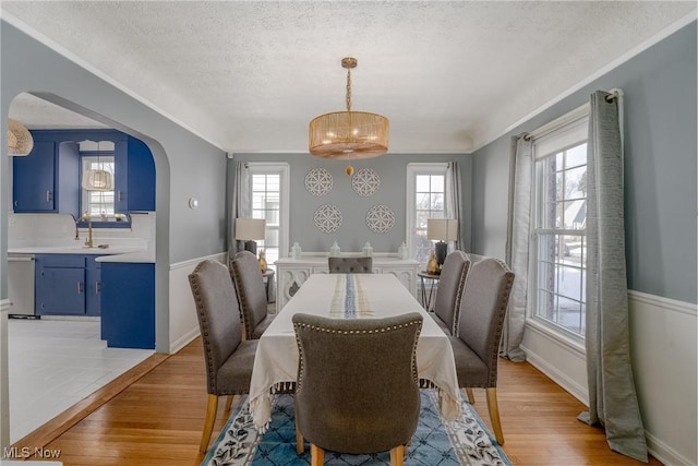 dining space with light wood-type flooring, baseboards, arched walkways, and a textured ceiling