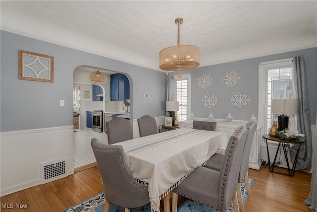 dining space featuring arched walkways, a textured ceiling, light wood-type flooring, and visible vents