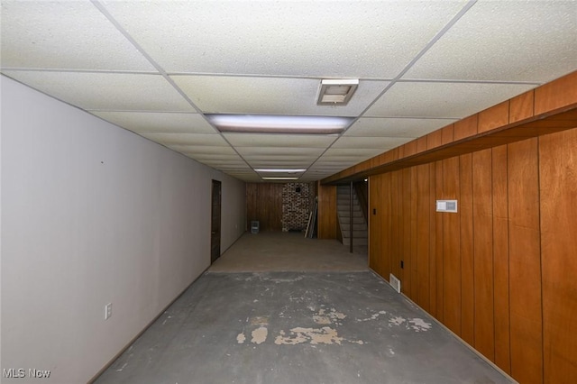 finished below grade area with stairway, wood walls, a drop ceiling, and visible vents