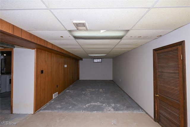 finished below grade area with a paneled ceiling, wooden walls, visible vents, and washer and dryer