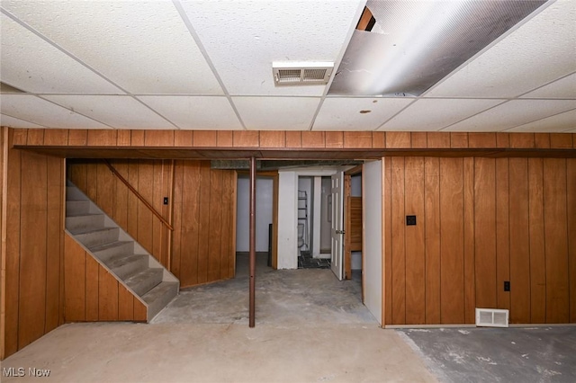 finished basement featuring a paneled ceiling, wooden walls, and visible vents