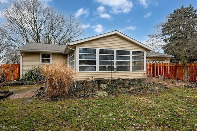 rear view of house featuring a yard, fence, and a sunroom