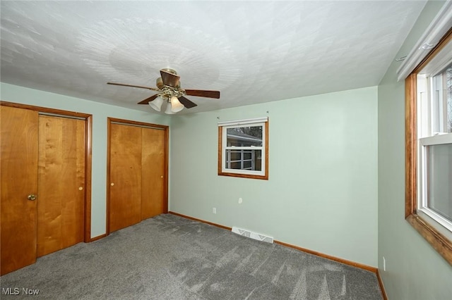unfurnished bedroom featuring carpet flooring, a ceiling fan, visible vents, baseboards, and two closets