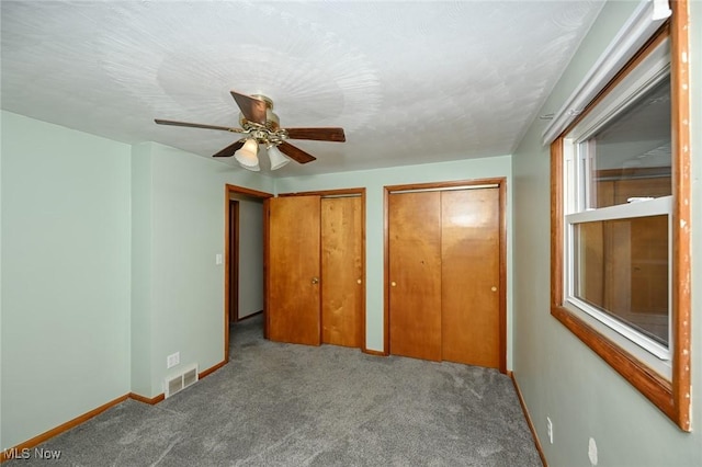 unfurnished bedroom with carpet floors, visible vents, baseboards, and two closets