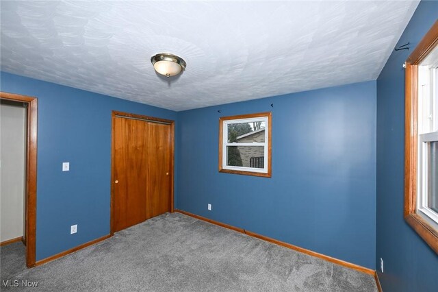 unfurnished bedroom featuring a textured ceiling, carpet floors, a closet, and baseboards