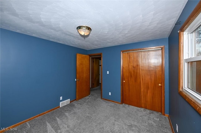 unfurnished bedroom with a textured ceiling, light carpet, visible vents, baseboards, and a closet