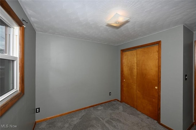 unfurnished bedroom with carpet, a textured ceiling, baseboards, and a closet