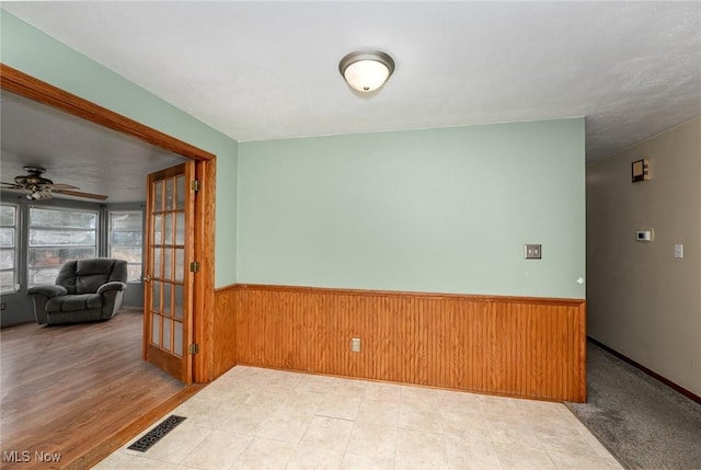 unfurnished room featuring french doors, visible vents, a ceiling fan, wainscoting, and wooden walls