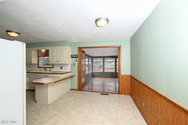 kitchen with a wainscoted wall, wood walls, a sink, visible vents, and light countertops