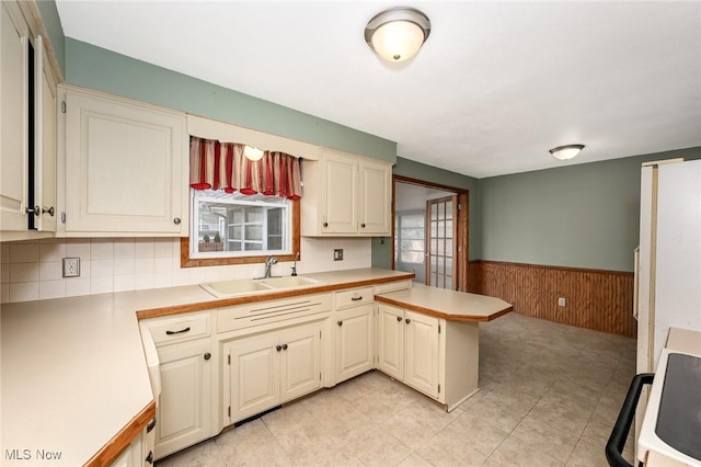kitchen with a peninsula, light countertops, a sink, and wainscoting