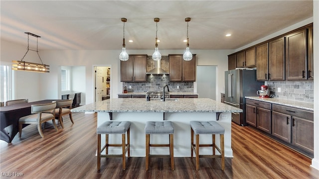 kitchen with high end fridge, pendant lighting, a center island with sink, and a sink