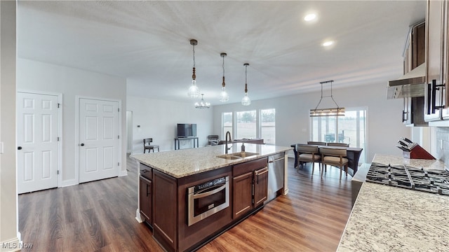 kitchen with pendant lighting, a center island with sink, appliances with stainless steel finishes, dark wood-type flooring, and a sink