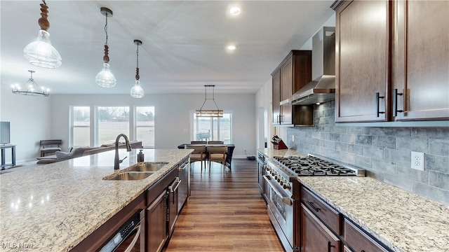 kitchen featuring stainless steel range, wall chimney exhaust hood, light stone countertops, pendant lighting, and a sink