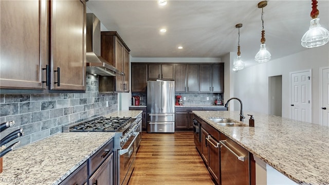 kitchen with wall chimney exhaust hood, appliances with stainless steel finishes, light stone countertops, dark brown cabinets, and a sink