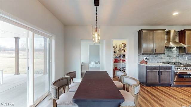 kitchen with decorative light fixtures, stainless steel stove, backsplash, light wood-type flooring, and wall chimney exhaust hood