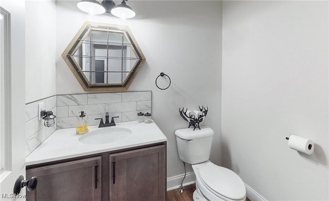 half bathroom with backsplash, toilet, vanity, wood finished floors, and baseboards